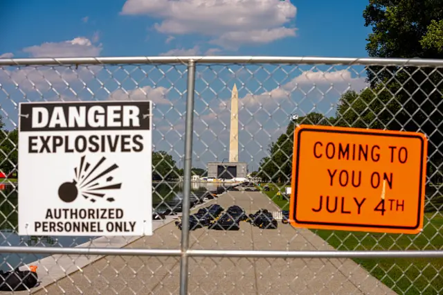 A fence near the Washington Monument has signs saying 'danger explosives' and 'coming to you on July 4'