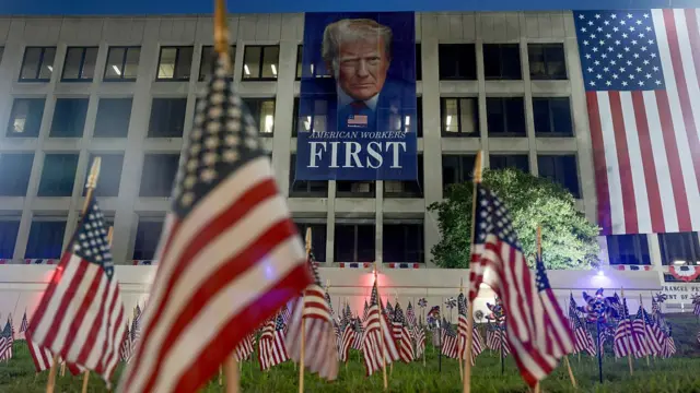 American flags are planted in the ground in front of a banner of U.S. President Donald Trump, hanging from the U.S. Department of Labor building, ahead of July 4th festivities on July 03, 2026,