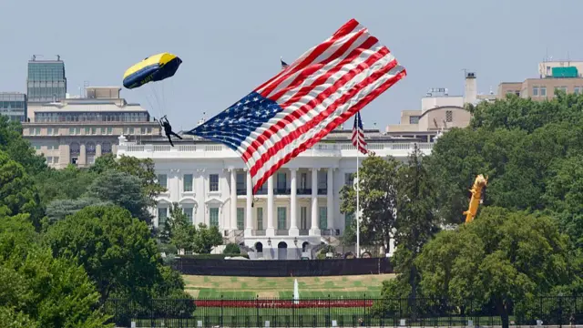 US Navy paratrooper carrying a US flag lands on the Ellipse just outside the White House (visible in the background surrounded by trees)