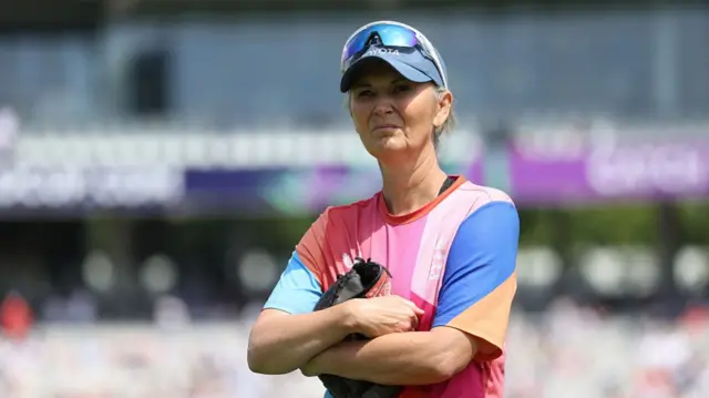 Charlotte Edwards, wearing a dark blue cap and a multi-coloured shirt, folds her arms and frowns