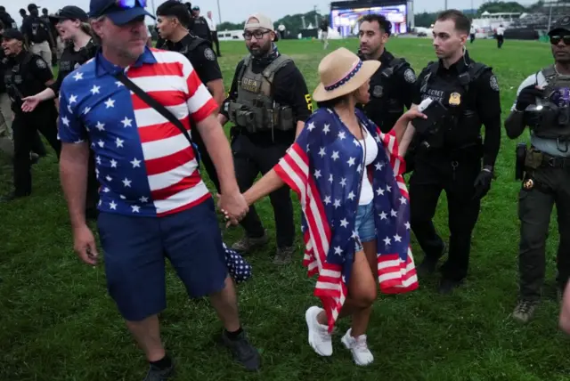 Two people wearing stars and stripes shirts speak with police on the National Mall