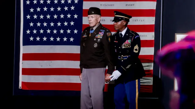 Retired U.S. Army Colonel and Medal of Honor recipient Paris D. Davis walks past Revolutionary-era "First American" flags while being accompanied to the stage as