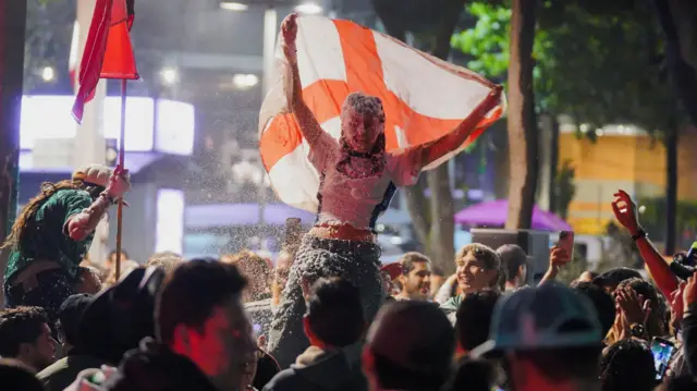 Female England fan raises a flag as she's lofted into the air