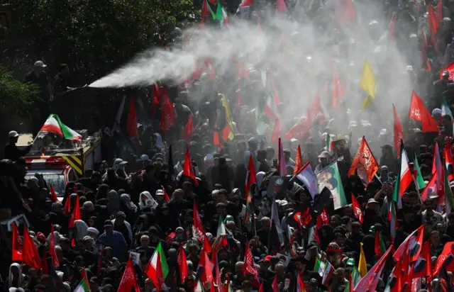 Crowds with flags for Iran being sprayed with water