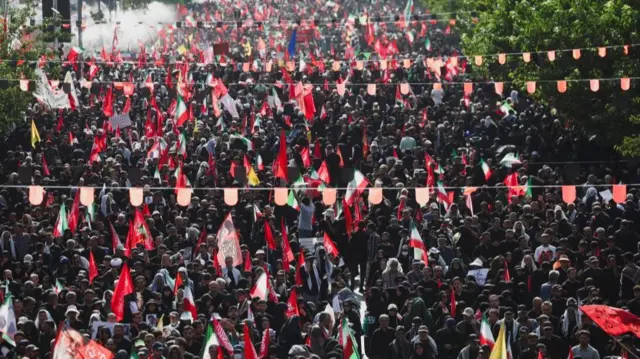 A landscape shot of a large crowd of people gathered under rows of flags