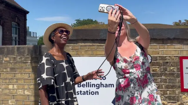 Local residents at Bellingham station take a selfie in front of a sign.
