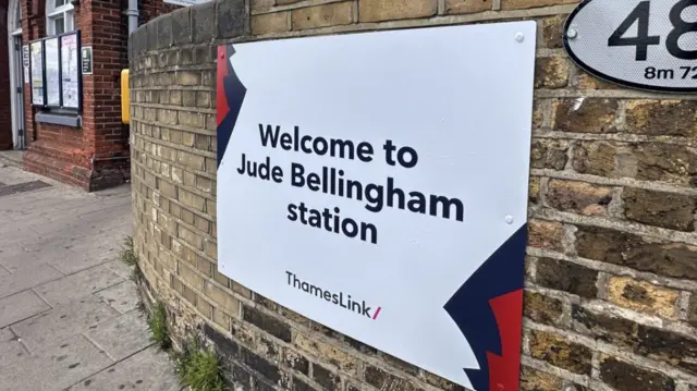 A sign reading 'welcome to Jude Bellingham station' on a wall outside a train station