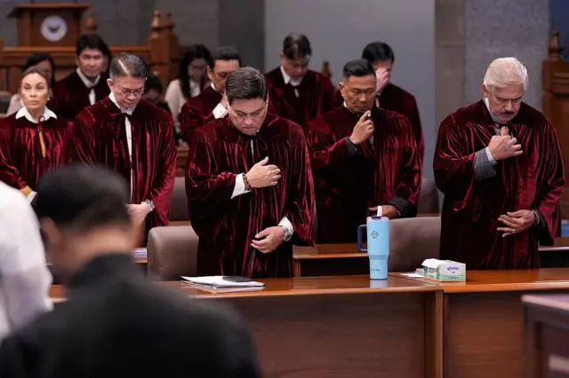 Senators in red robes lower their heads and pray in the Senate building in Manila