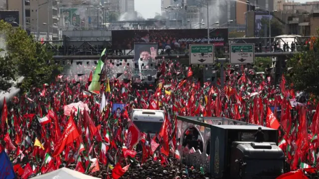 Two vehicles make their way through crowds of people holding flags