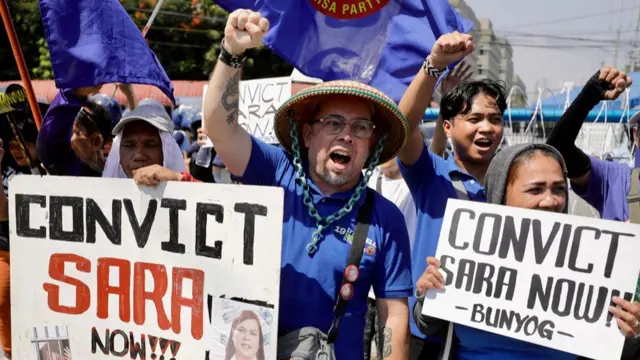 Protesters in blue shirts holding signs that read: Convict Sara Now