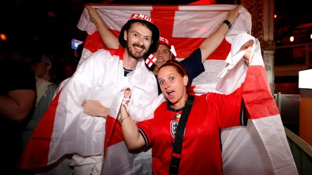 Three fans draped in the England flags pose for the camera.