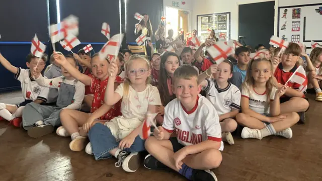 A group of primary school students in Castleway Primary waving England flags