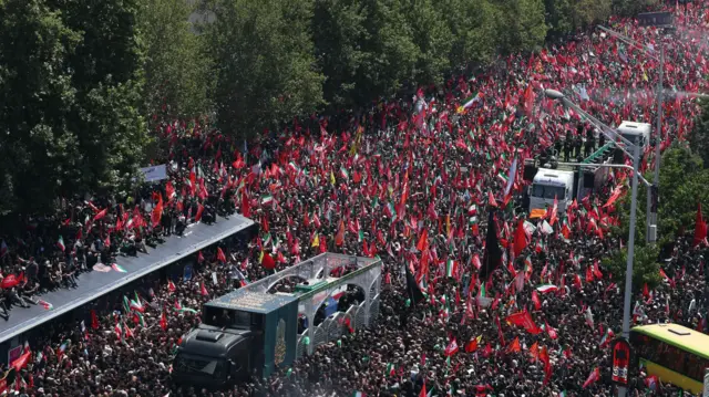 A vehicle carrying the coffins of Khamenei and family members makes its way through crowds of people and is followed by another vehicle