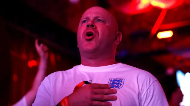 A man sings while holding his hand to the England football team's logo on his chest.
