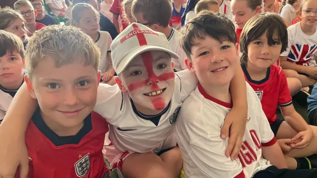 Children wear England shirts in a school hall