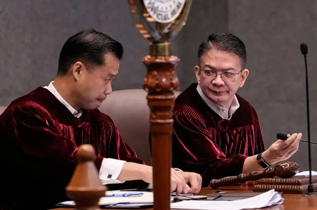 Two men in red robes sit at a stately wooden desk in the Philippines Senate hall