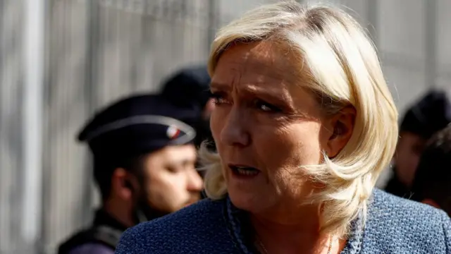 Marine Le Pen looks to her right while walking outside. Her mouth is open and she is wearing a blue dress.