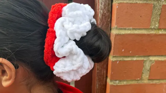 The back of a young girl's head is shown, with a red and white scrunchie tied around her hair bun.