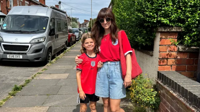 Jess Clarke and her son Wren pose together on the street. They are both wearing England tops