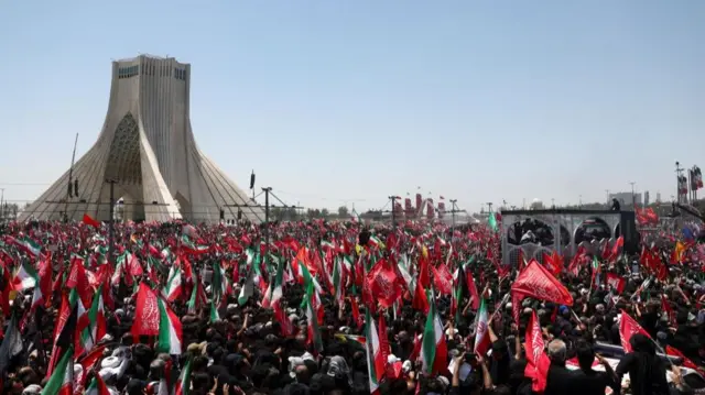 The vehicle carrying Khamenei's coffin progresses through a crowd of people waving flags