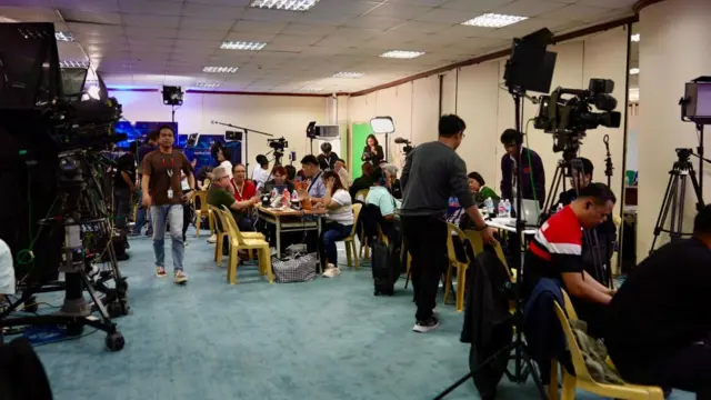 Cameras all lined up in a room with tables and chairs