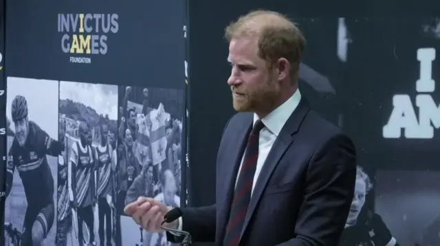 Prince Harry speaking in front of Invictus Games promotional banner