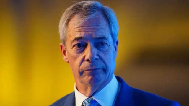 Nigel Farage is pictured in a head and shoulders portrait, looking off to one side with a serious expression and wearing a suit and tie.