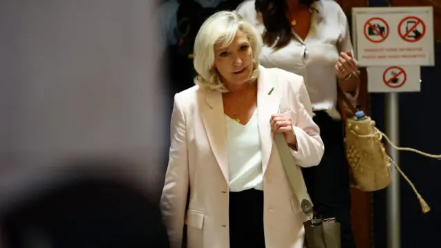 Marine Le Pen leaves a courthouse while wearing a pink blazer.