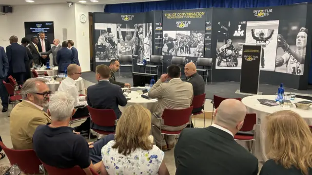 People sat around tables in front of Invictus Games signage