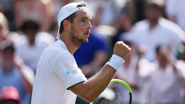 Jan-Lennard Struff, wearing a white t-shirt and backwards white cap, raises a clenched right fist
