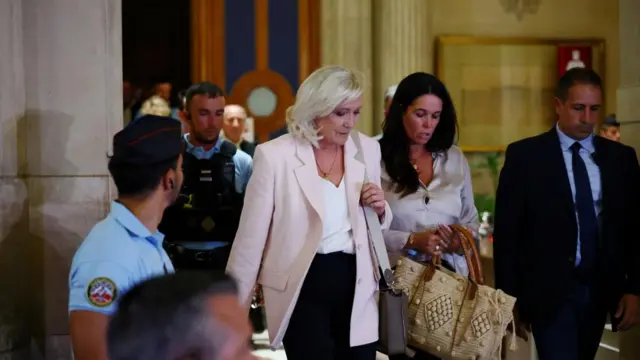 Le Pen walks out of a building escorted by police and other people