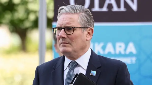 Keir Starmer, a man, wearing glasses, a dark blazer, grey tie and shirt.
