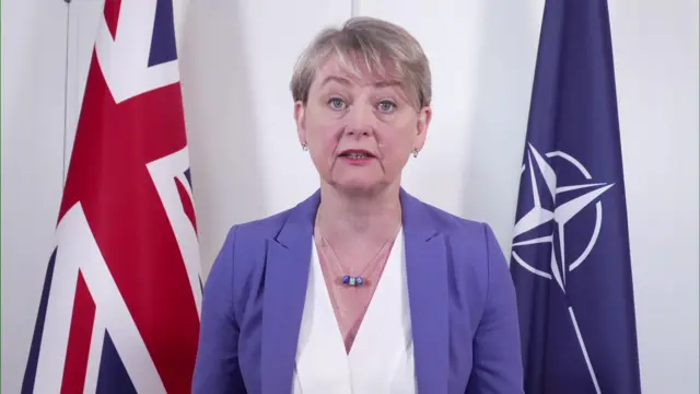 Yvette Cooper in a blue jacket in front of UK and Nato flags