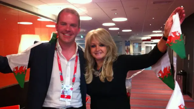 Huw Thomas and Bonnie Tyler holding Welsh flag bunting smiling at the camera