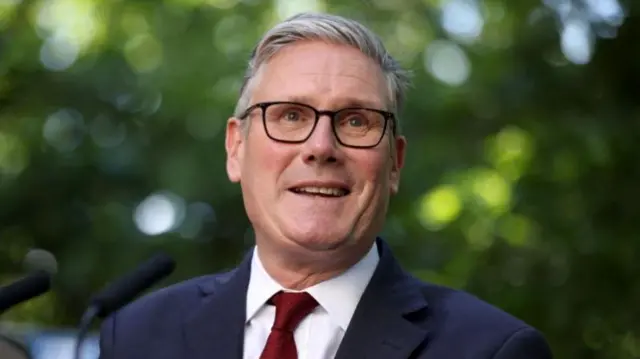 Keir Starmer is pictured speaking against a background of greenery.