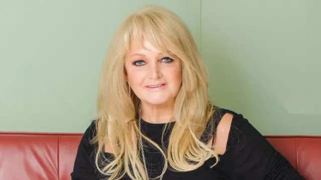 Bonnie Tyler sitting on a red leather sofa