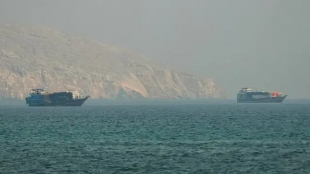Tow ships visible on top of a turquoise sea. Coast is visible in the background beyond a layer of fog.