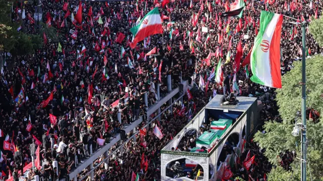 Crowds of mourners surround the convoy carrying the coffins of Ali Khamenei.
