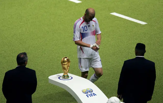 French midfielder Zinedine Zidane (C) walks past the World Cup trophy being guarded by security as he leaves the pitch