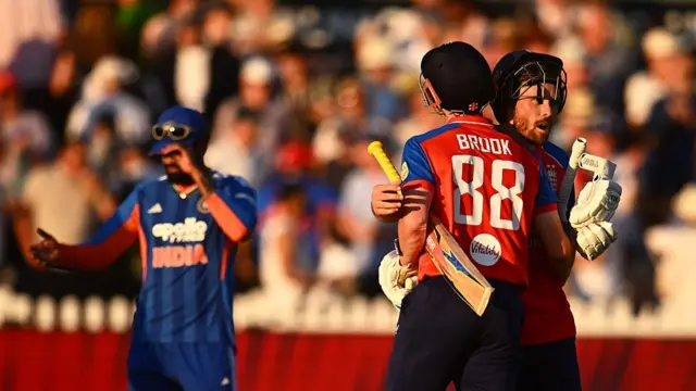 Phil Salt (right, facing the camera) and Harry Brook, both wearing red England shirts with blue sleeves, embrace at the end of the match