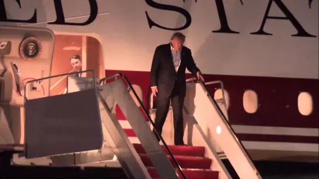 Trump wears a black suit and walks down red carpeted steps off Air Force One