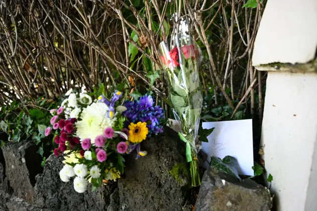 Flowers and a card left on the wall of the house