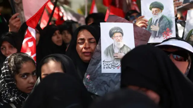 Several women seen at the burial ceremony of Iran's former supreme leader. Some are holding artwork of him.