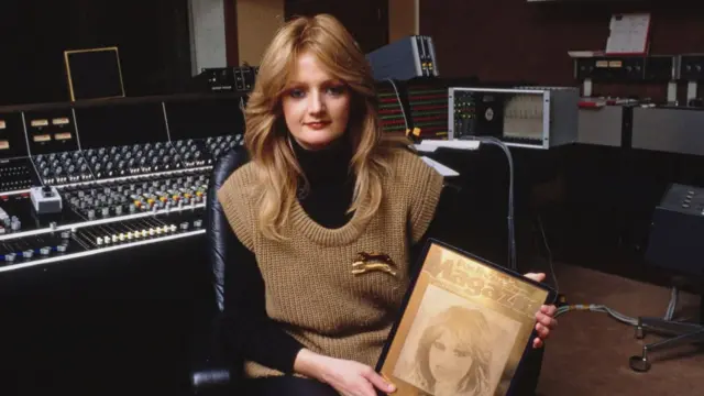 Bonnie Tyler is pictured in a recording studio holding a framed copy of a magazine cover.