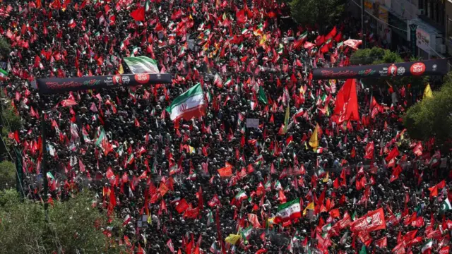 Hundreds of people carrying red flags or Iranian flags line the streets during the last day of mourning for the former Iranian supreme leader Ali Khamenei