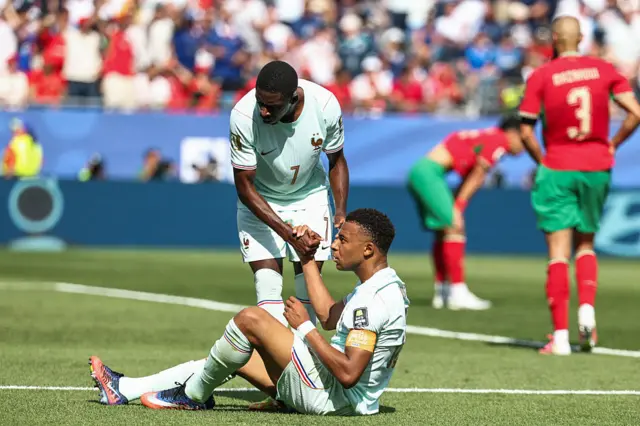 Mbappe is comforted after his penalty miss as Morocco players celebrate in the background
