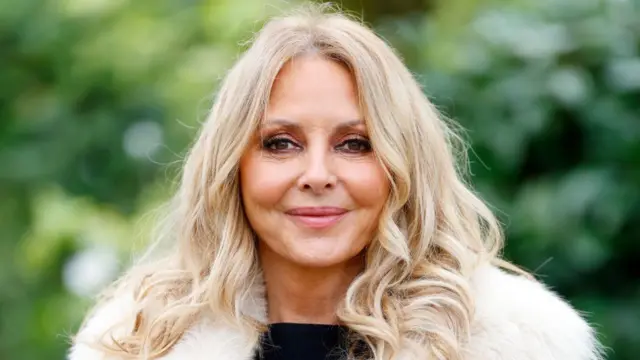 Carol Vorderman is shown smiling to the camera against a garden background.