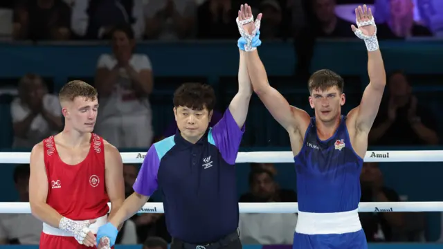 Patris Mughalzai, wearing England's blue boxing jersey, has his hand held up by the referee after his gold medal final win