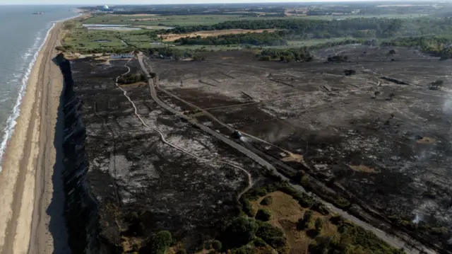 Aerial shot of Dunwich Heath showing the expanse of the wildfire. Fields next to the beach are completely blackened out by the fire, as grey smoke rises in some areas
