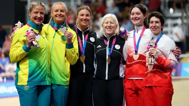 All six athletes show their medals to the camera with their arms around each other